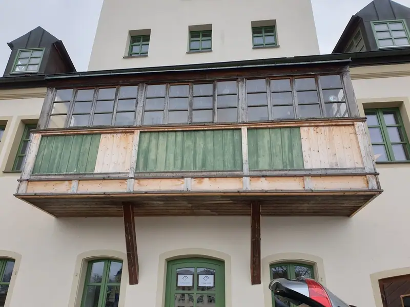 Verkleideter Holzbalkon mit Sprossenfenstern und grünen Füllungen an einer Altbaufassade