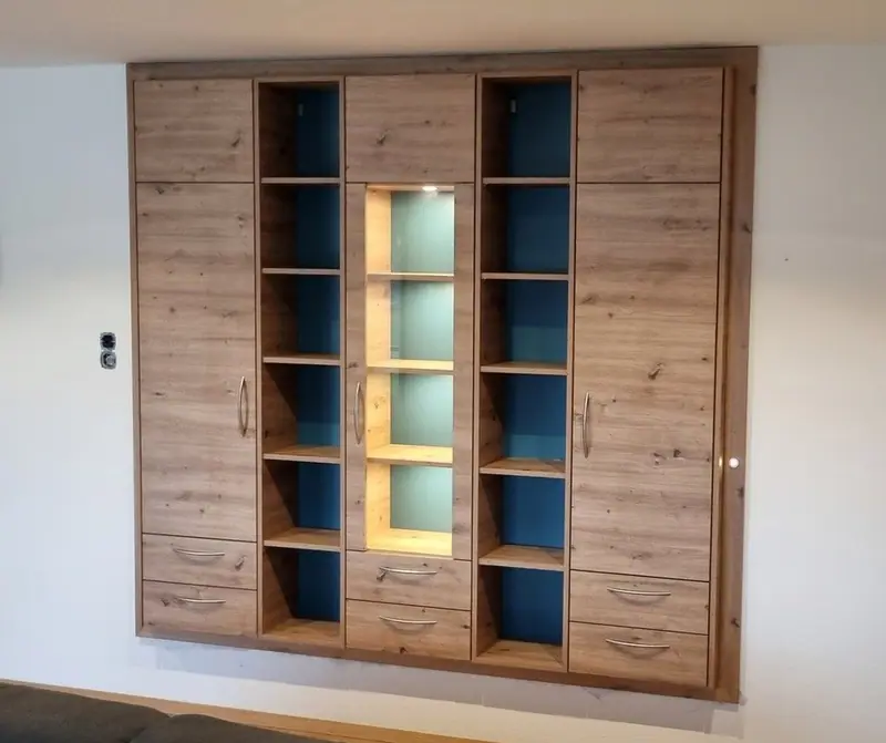 Raumhoher Wandschrank in Holzoptik mit beleuchteten offenen Regalfächern und Schubladen